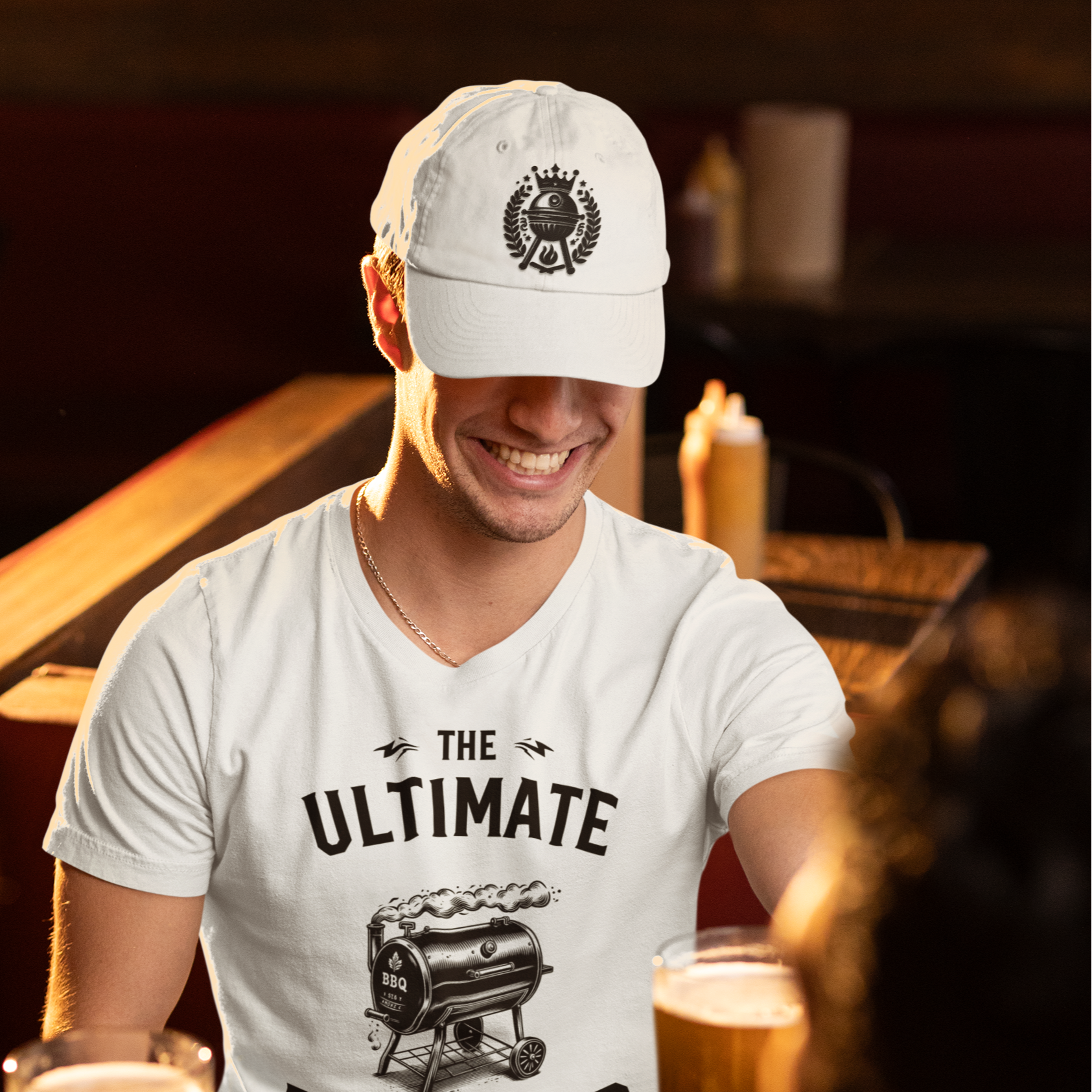 Man wearing a 'The Ultimate BBQ Master' shirt at a bar with drinks and food. Alpha bbqwear cap