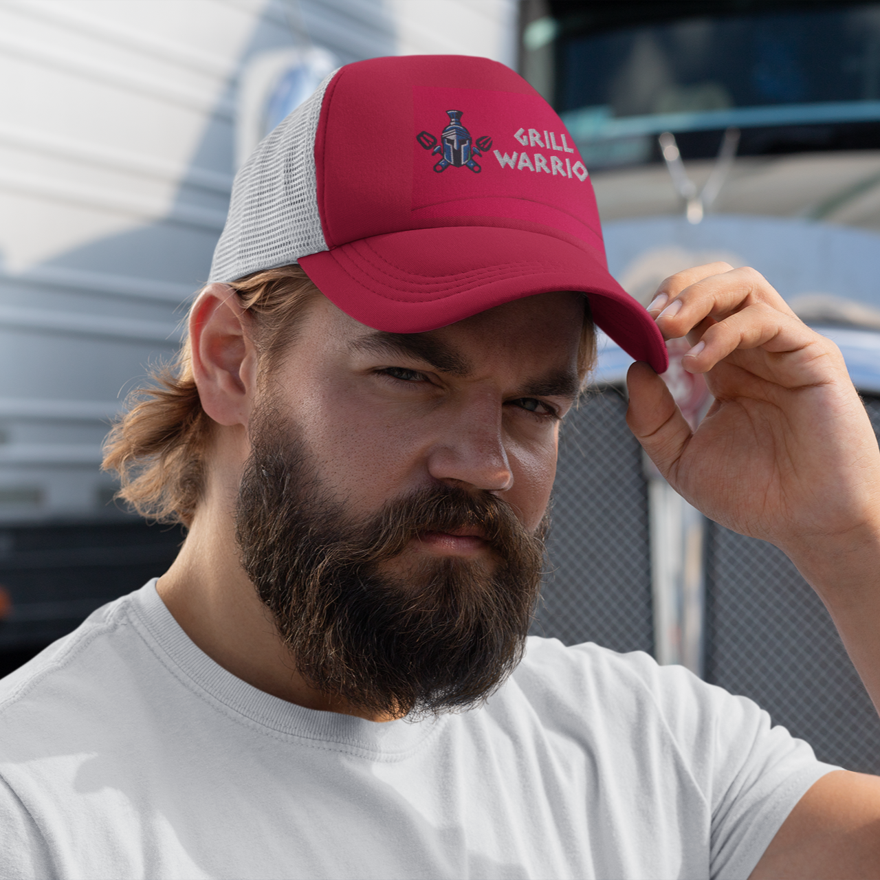 Man wearing a red cap with a logo in front of a large truck Alpha bbqwear cap